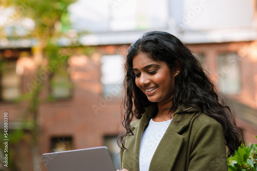 Brunette indian woman smiling while working with laptop on city street © Drobot Dean