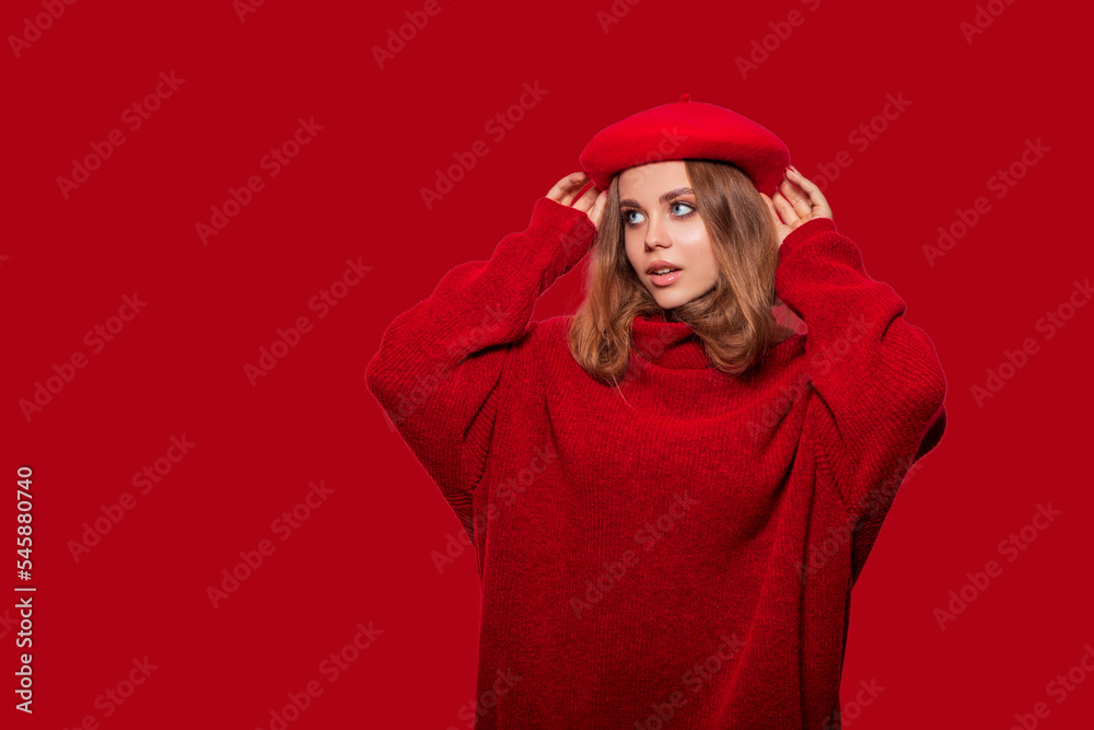 Fototapeta premium Beautiful girl in red clothes isolated on colorful red background. Isolated. Cute girl wears a beret with delight looks away from amazement or from a pleasant surprise 