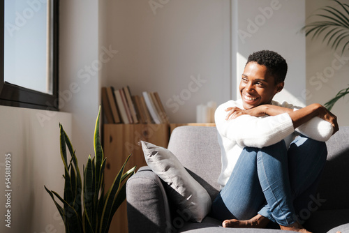 Smiling relaxed woman sitting on the couch at home looking out of window