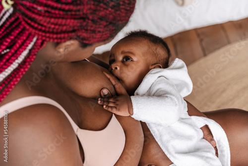 Young african american woman breastfeeding her baby in bedroom