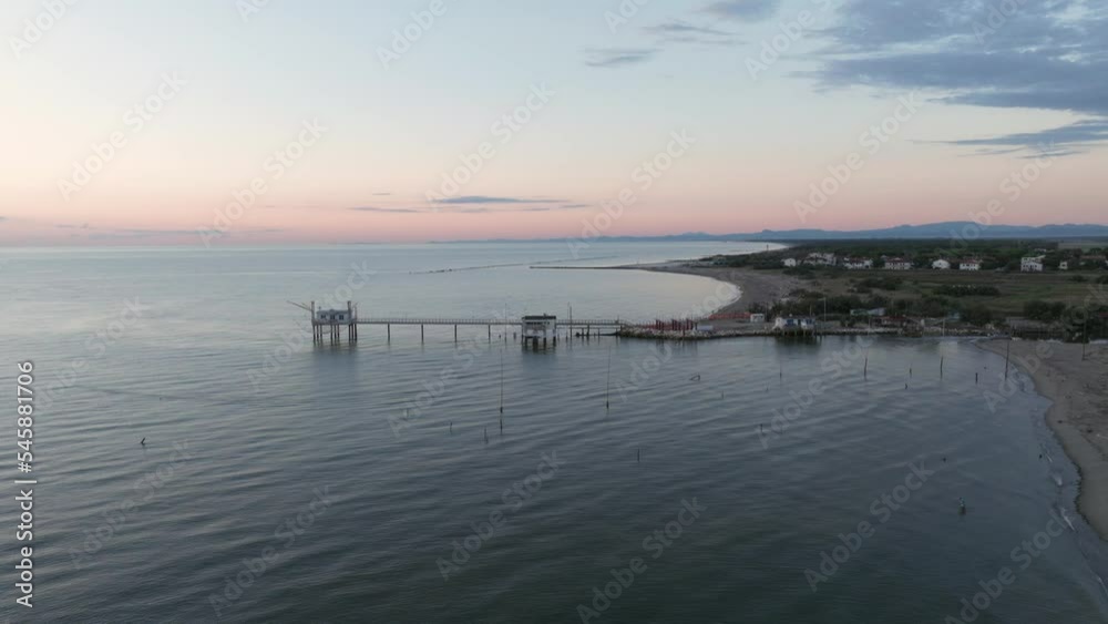 Aerial view slow motion of fishing huts on shores of estuary at sunset,italian fishing machine, called 