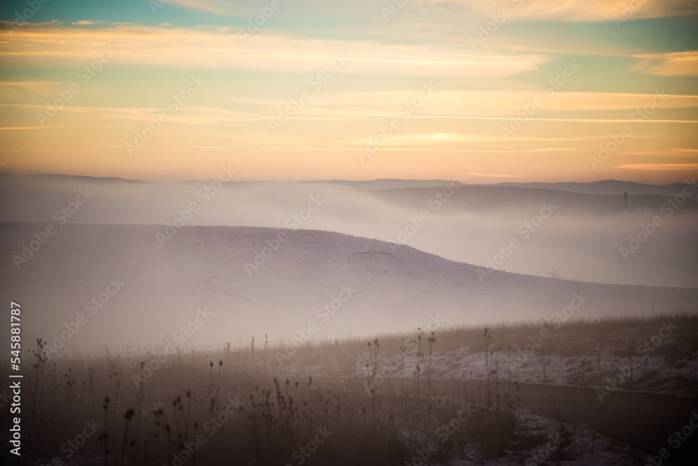 moody winter landscape with fog at sunset