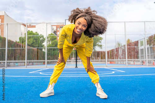 Happy young woman with Afro hairstyle bending on sports court photo