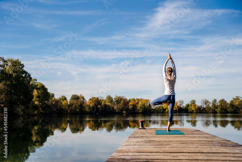 Woman practicing yoga on jetty at lake photo