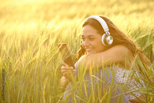 Happy woman at sunset listening to music from phone