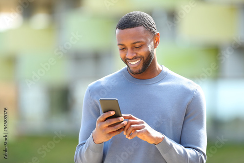 Happy black man checks cell phone walking