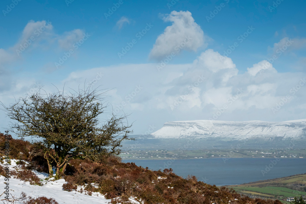 Winter nature scene in county Sligo, Ireland. Slope of a hill covered with snow and blue cloudy sky. Cold season. Stunning Irish nature landscape. Benbulben mountain in the background.