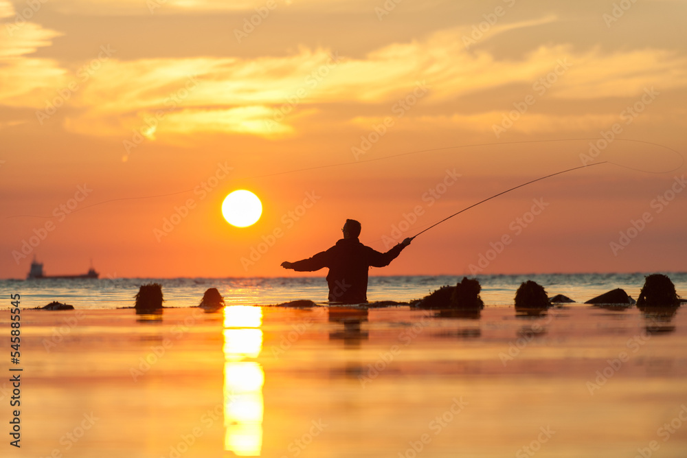 Rear view of man fishing in sea at sunset