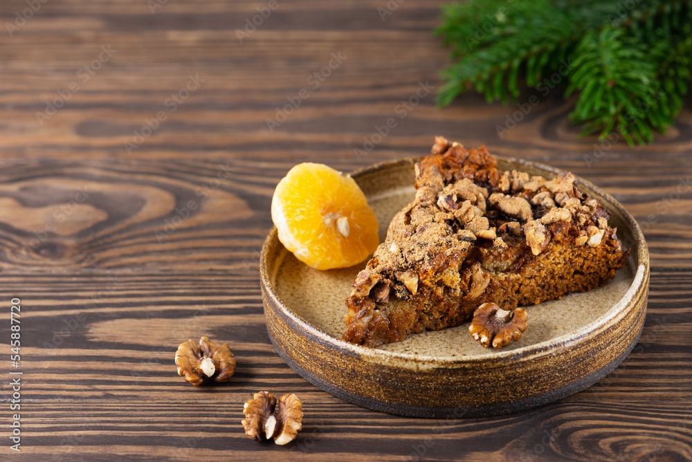 A piece of homemade tangerine pie with walnuts and a spruce branch on a brown wooden table, sugar, gluten and lactose free.