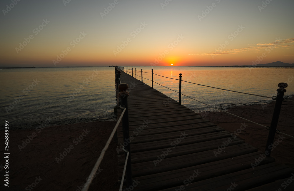 Amazing sunrise landscape from the sea with the silhouette of a wooden pontoon deck in foreground. Beautiful photo at the seaside. Holiday by the sea.