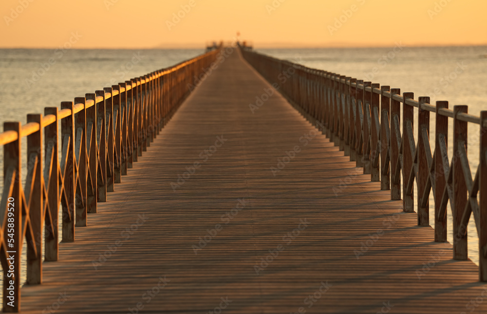 A wooden pontoon deck on a sea side beach during summer sunrise. A wooden pontoon deck on a sea side beach during summer sunrise.