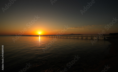 Amazing sunrise landscape from the sea with the silhouette of a wooden pontoon deck in foreground. Beautiful photo at the seaside. Holiday by the sea. © Dragoș Asaftei