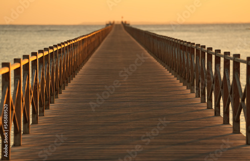 A wooden pontoon deck on a sea side beach during summer sunrise.