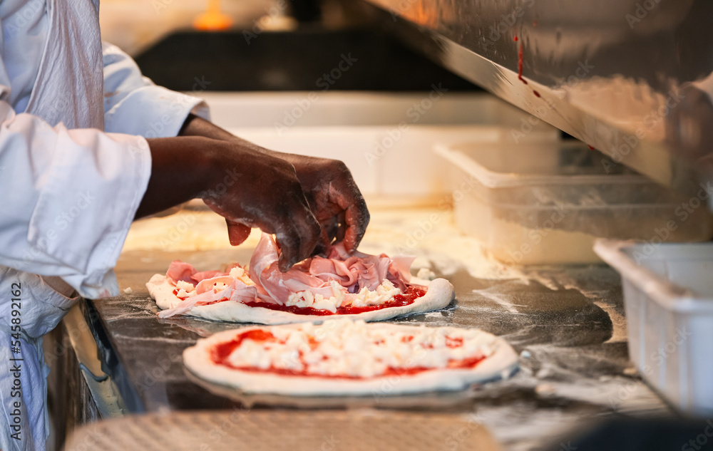 A chef prepares a prosciutto and champignons pizza inside an Italian restaurant. Photo with the moment when he adds the ingredients.A chef prepares a prosciutto and champignons pizza inside an Italian