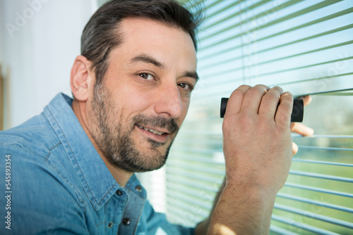 Fotografi excited man spying through the window blinds with binoculars