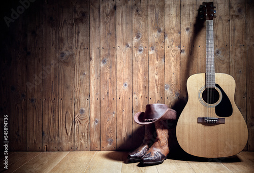 Acoustic guitar, cowboy hat and boots against blank wooden plank panel grunge background with copy space photo