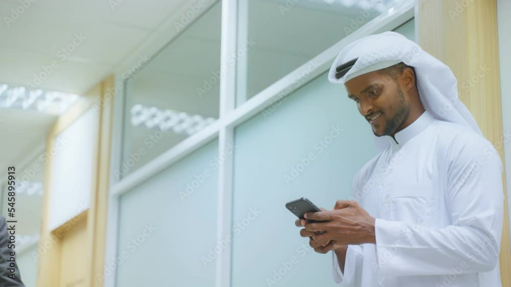 Arab Businessman using smartphone while standing in corridor of office Arab Businessman using smartphone while standing in corridor of office