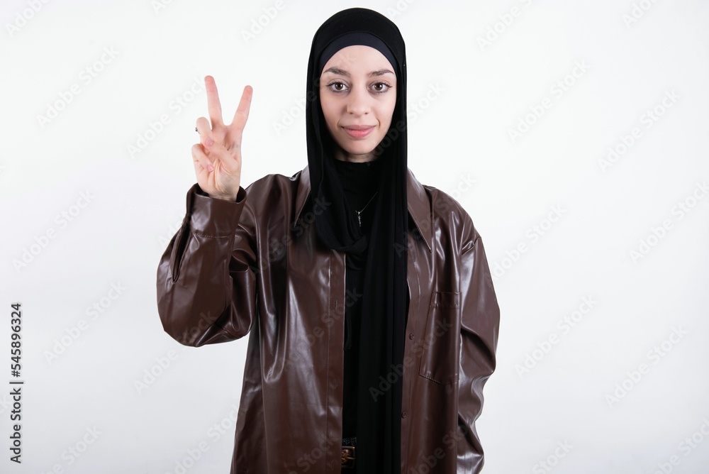 young beautiful muslim woman wearing hijab and leather jacket over white background showing and pointing up with fingers number two while smiling confident and happy.