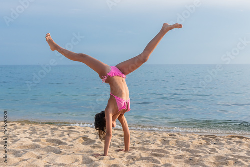фотографія A child on the beach does sports and performs gymnastic exercises against the background of the sea