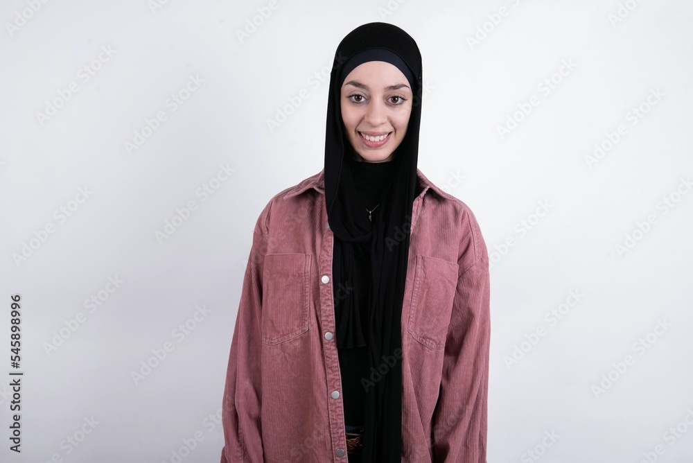 young beautiful muslim woman wearing hijab and pink jacket over white background with nice beaming smile pleased expression. Positive emotions concept young beautiful muslim woman wearing hijab and pink jacket over white background with nice beaming smile pleased expression. Positive emotions concept