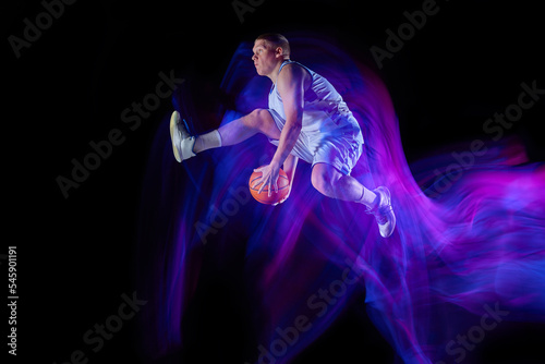Studio shot of young active athlete, male basketball player in sports uniform in motion and action with ball isolated over dark background in glow neon light © master1305