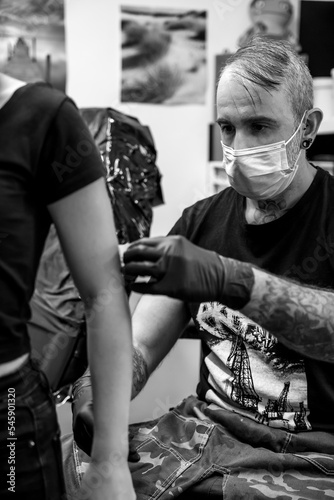 Tattoo artist placing the pattern on the arm of an unrecognizable woman - work and art concept