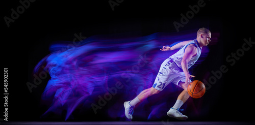 Professional basketball player in action with ball isolated on black background in neon light filter. Dribbling. Sport, energy, skills, team competition. Flyer