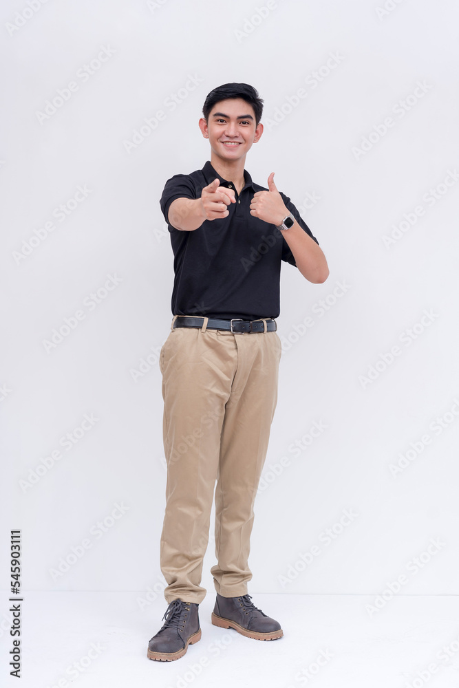 A friendly asian man points to the camera while smiling. Endorsing someone, making the thumbs up sign. Isolated on a white background. A friendly asian man points to the camera while smiling. Endorsing someone, making the thumbs up sign. Isolated on a white background.