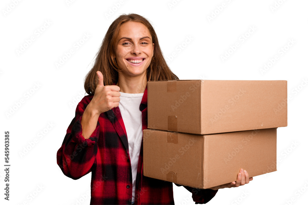 Young caucasian woman moving while picking up a box full of things isolated smiling and raising thumb up Young caucasian woman moving while picking up a box full of things isolated smiling and raising thumb up