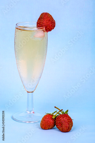 A misted glass of champagne and fresh strawberries on a blue background