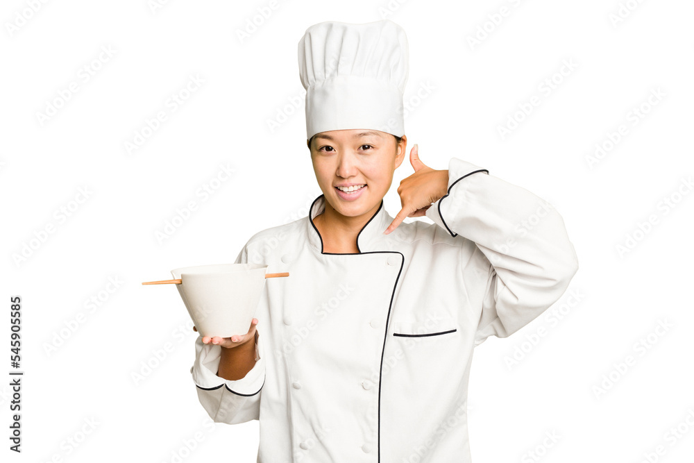 Young chef asian woman holding a bowl of ramen isolated showing a mobile phone call gesture with fingers. Young chef asian woman holding a bowl of ramen isolated showing a mobile phone call gesture with fingers.