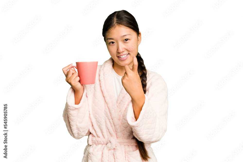 Young asian woman wearing a pajama holding a cup isolated pointing with finger at you as if inviting come closer. Young asian woman wearing a pajama holding a cup isolated pointing with finger at you as if inviting come closer.