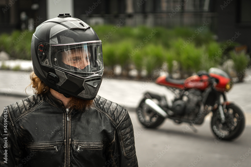 Biker in helmet stands in front of motorcycle and looks away