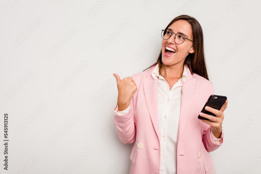 Business caucasian woman holding a mobile phone isolated on white background points with thumb finger away, laughing and carefree. Business caucasian woman holding a mobile phone isolated on white background points with thumb finger away, laughing and carefree.