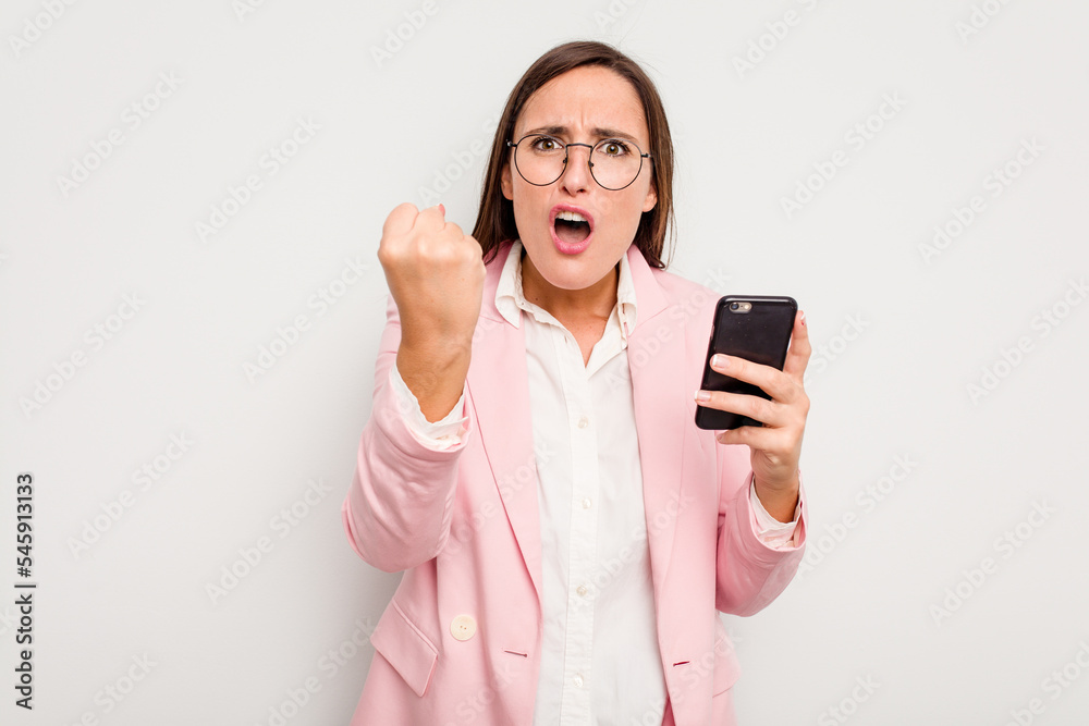 Business caucasian woman holding a mobile phone isolated on white background showing fist to camera, aggressive facial expression. Business caucasian woman holding a mobile phone isolated on white background showing fist to camera, aggressive facial expression.