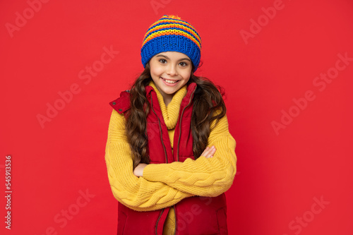 happy teen girl in knitted winter hat and down vest on red background, portrait
