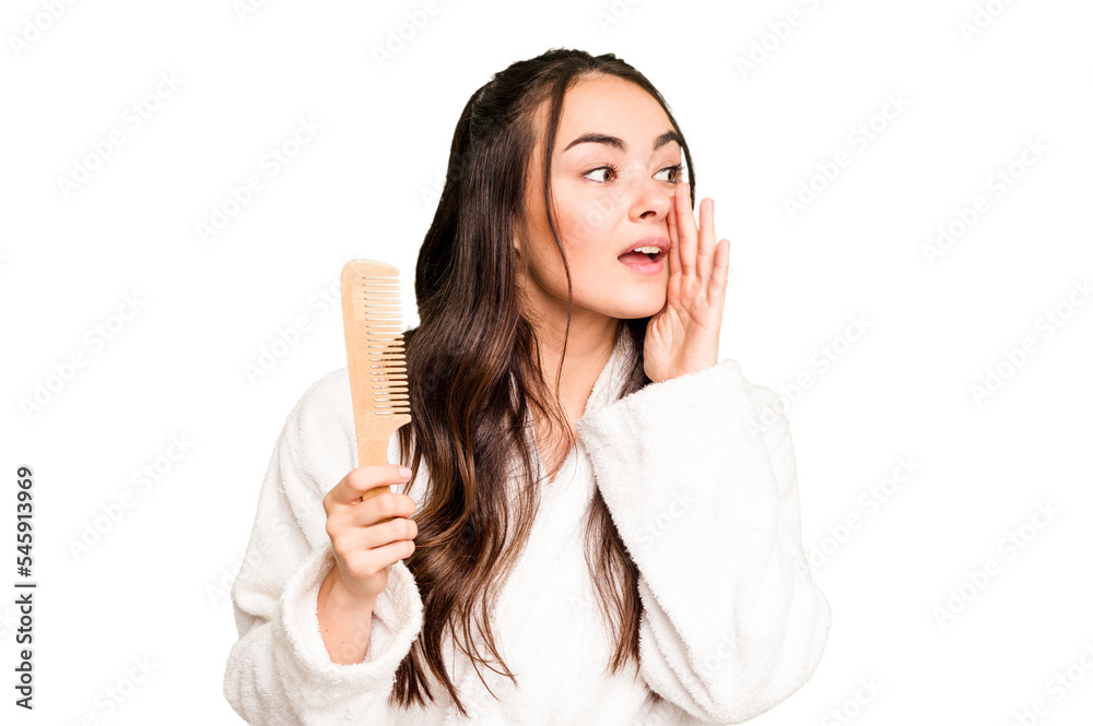 Young caucasian woman holding a hairbrush isolated on green chroma background shouting and holding palm near opened mouth.