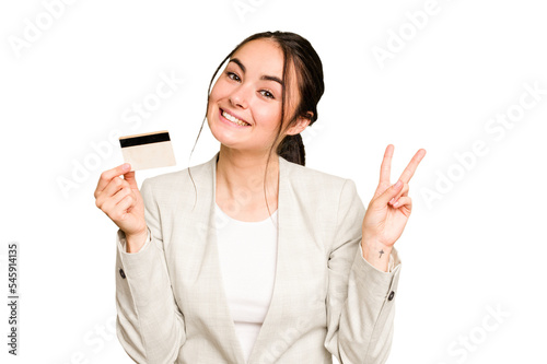 Young caucasian woman holding a credit card isolated on green chroma background joyful and carefree showing a peace symbol with fingers. photo