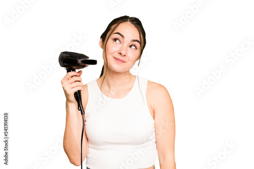 Young caucasian woman holding a hairdryer on green chroma background dreaming of achieving goals and purposes