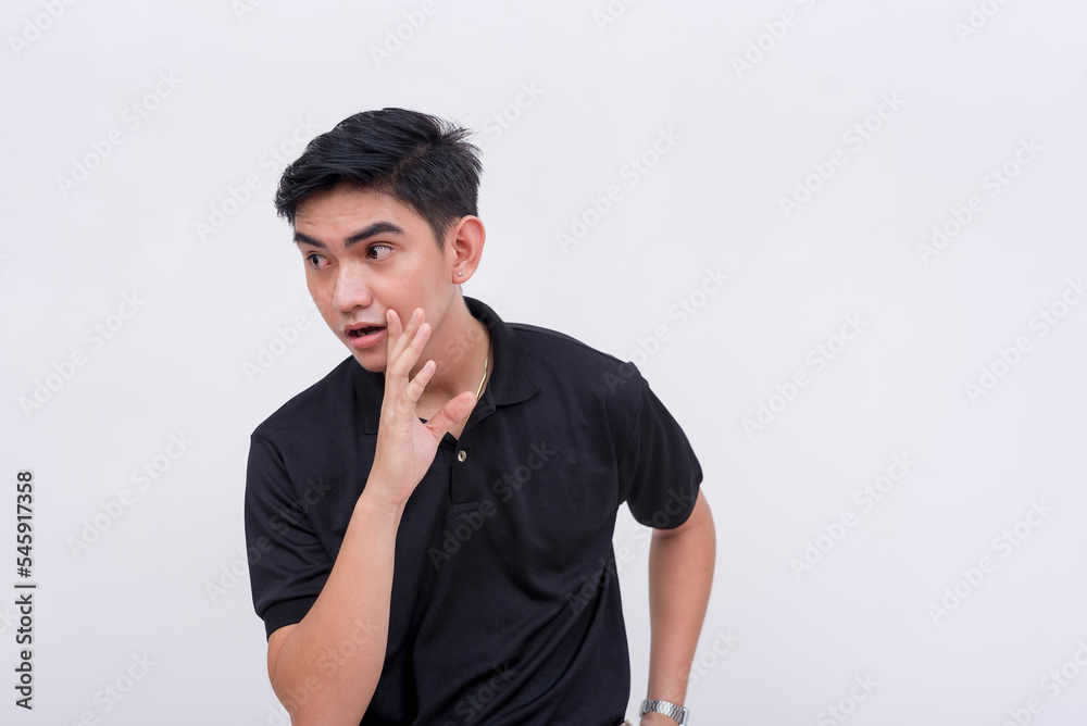 A young man shares a secret confidential story or rumor, whispering while covering his mouth. Looking around feeling wary. Isolated on a white background. A young man shares a secret confidential story or rumor, whispering while covering his mouth. Looking around feeling wary. Isolated on a white background.