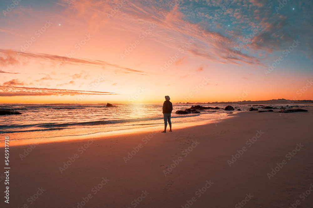 silhouette of a person standing on the shore of the beach looking at and enjoying a beautiful sunset on the horizon