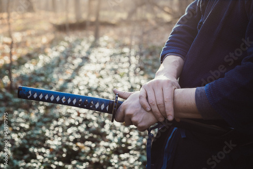 Close up hand with weapon concept photo. Man holding katana. Side view photography with autumn forest on background. High quality picture for wallpaper, travel blog, magazine, article
