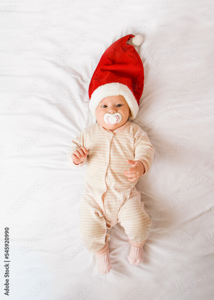 baby in a Santa hat and with a pacifier lies on the bed baby in a Santa hat and with a pacifier lies on the bed
