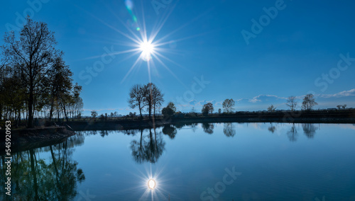 Landscape of lake with sun reflection which is on blue sky, Silhouette of trees in the background