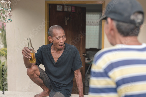 A man enjoying a lively discussion with an old friend while enjoying a cold bottle of beer by the veranda. Older men relaxing and being carefree. photo