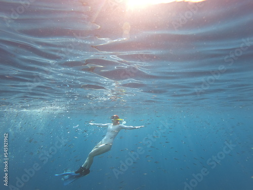 Woman snorkeling in light blue ocean with many fish