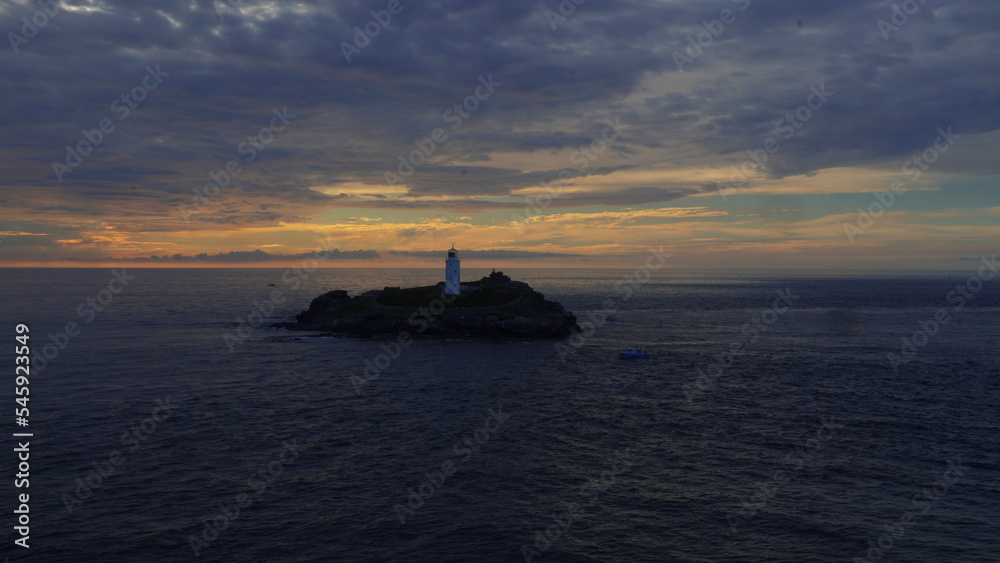Leuchtturm auf Felsen im Meer mit dramatischem Sonnenuntergang