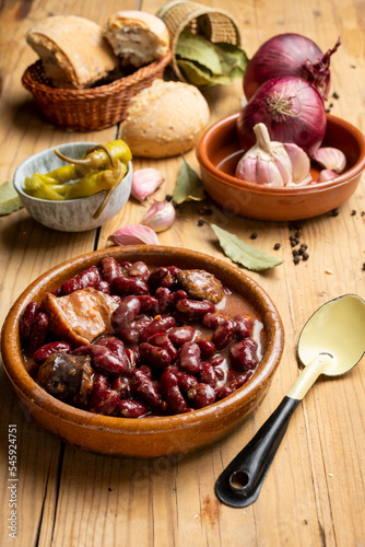 Top view of red bean stew on rustic wooden table with spoon, green chillies, garlic, onions, bay leaf and bread, vertical
