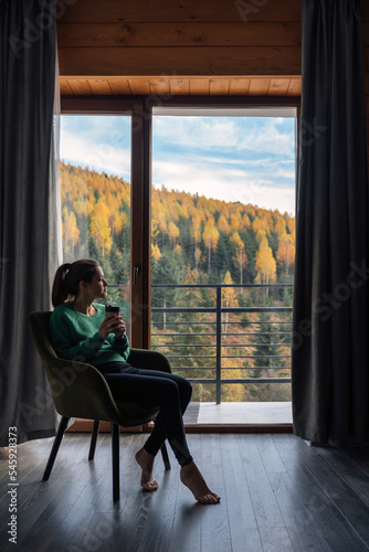 Wallpaper Mural Woman in green sweater sitting with coffee near panoramic window at modern living room with stunning view on autumn forest mountains Torontodigital.ca