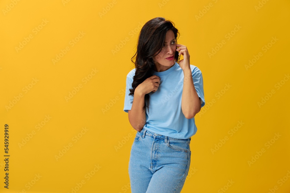 Woman blogger with a phone in her hands in a blue t-shirt and jeans on a yellow background smile signs gestures symbols, online communication and video call, copy space, free background